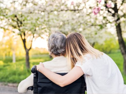 Young woman leaning affectionately against an older woman in a wheelchair